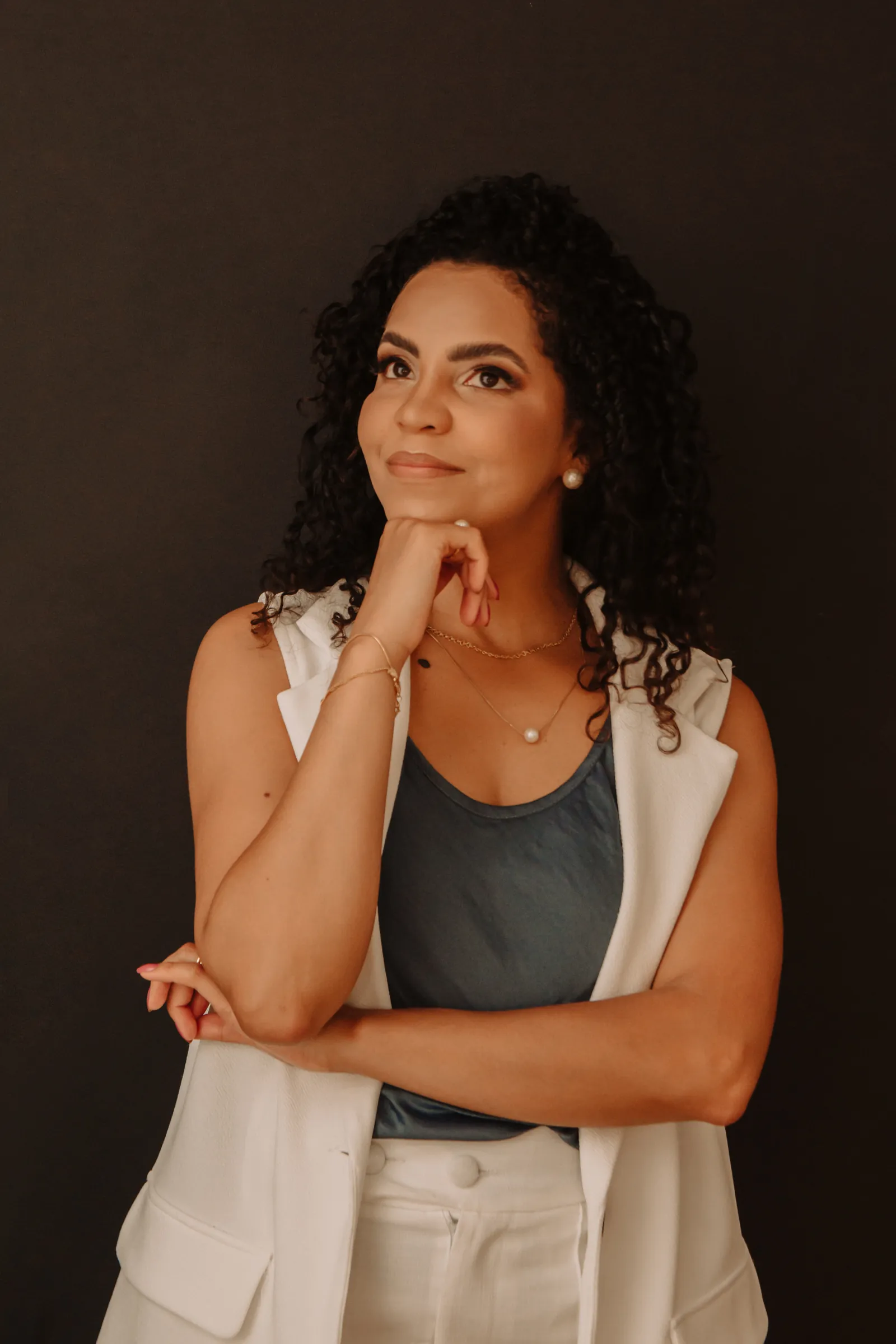 Amanda Lima de colete branco, olhando para o alto com a mão no queixo