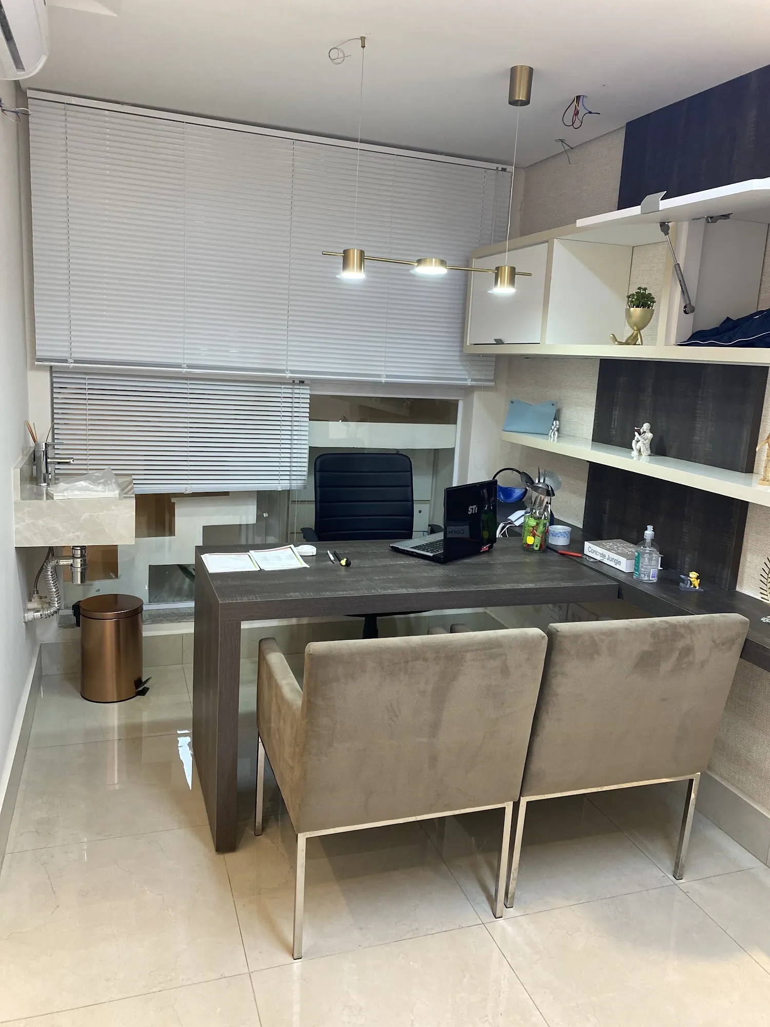 Sala de atendimento com mesa, duas poltronas bege e prateleiras