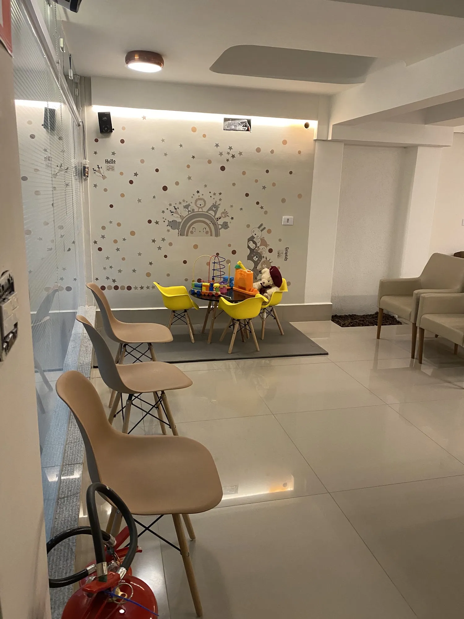 Sala de espera com cadeiras bege, poltronas e cantinho infantil com cadeiras amarelas